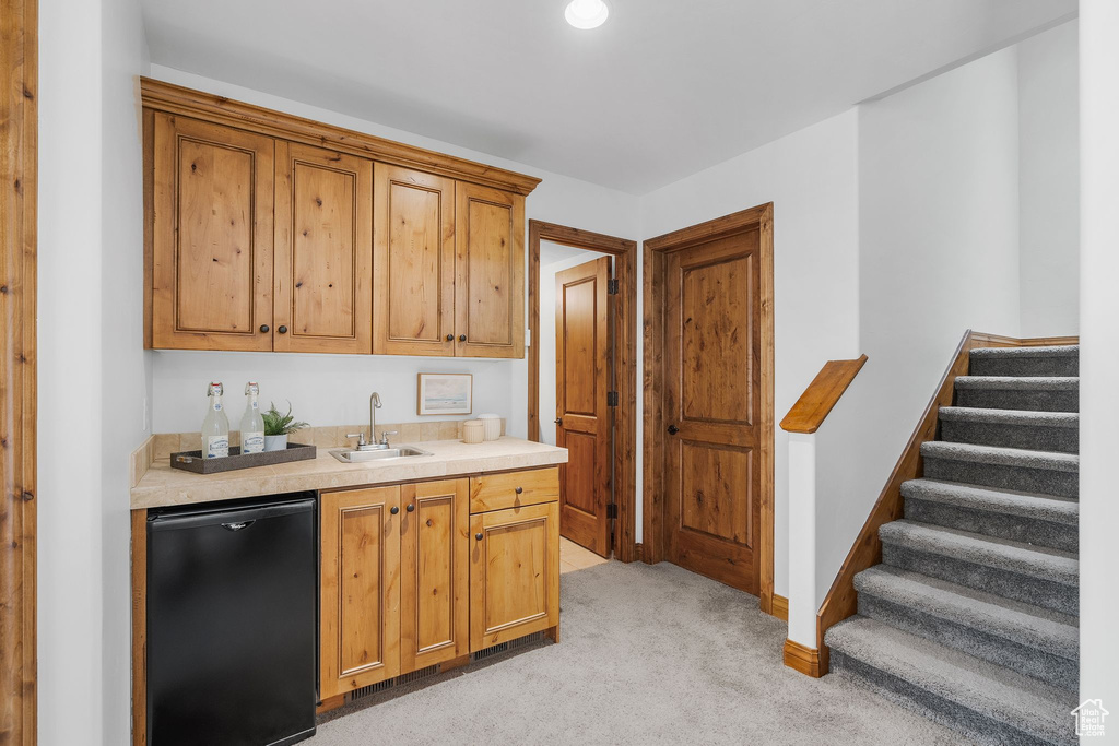 Kitchen with dishwashing machine, light countertops, light colored carpet, and brown cabinetry