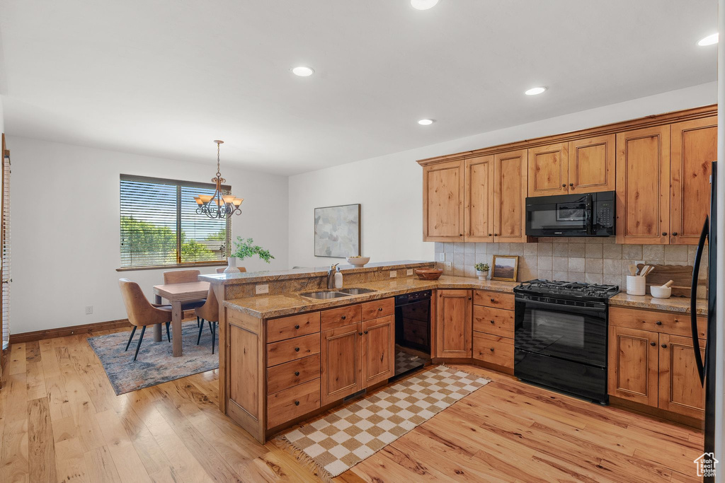 Kitchen with black appliances, a peninsula, light wood-style floors, decorative backsplash, and decorative light fixtures
