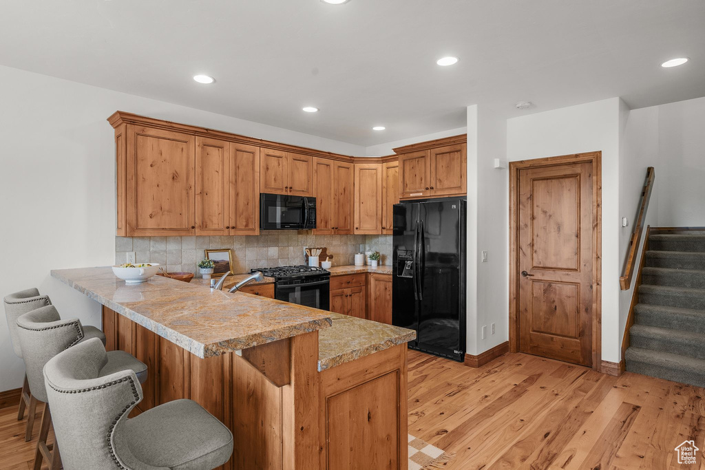 Kitchen featuring black appliances, light countertops, light wood-style flooring, a peninsula, and backsplash