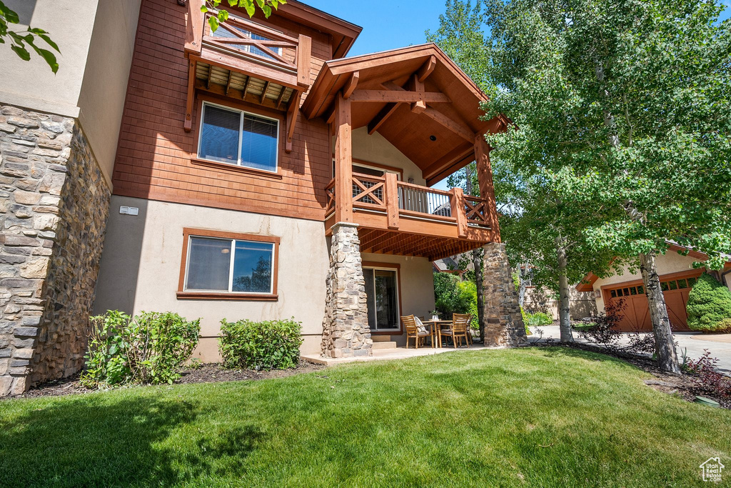 Back of house featuring a balcony, stucco siding, a yard, and stone siding