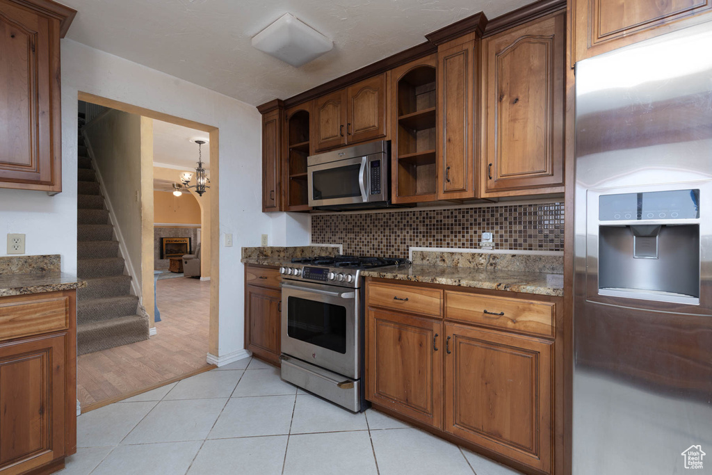 Kitchen featuring tasteful backsplash, light tile patterned floors, stone counters, appliances with stainless steel finishes, and open shelves