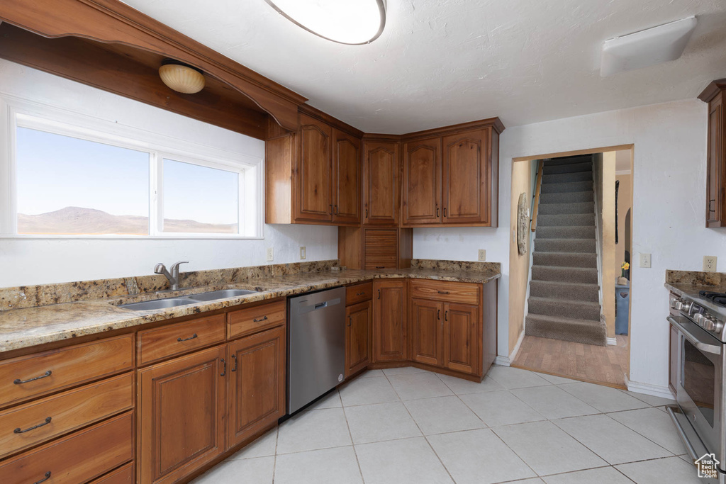 Kitchen featuring brown cabinets, a sink, stainless steel appliances, light tile patterned flooring, and light stone countertops