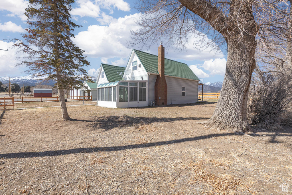 Rear view of house featuring fence, a chimney, a sunroom, and metal roof