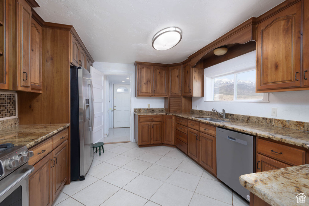 Kitchen featuring a sink, stainless steel appliances, brown cabinets, and light stone countertops