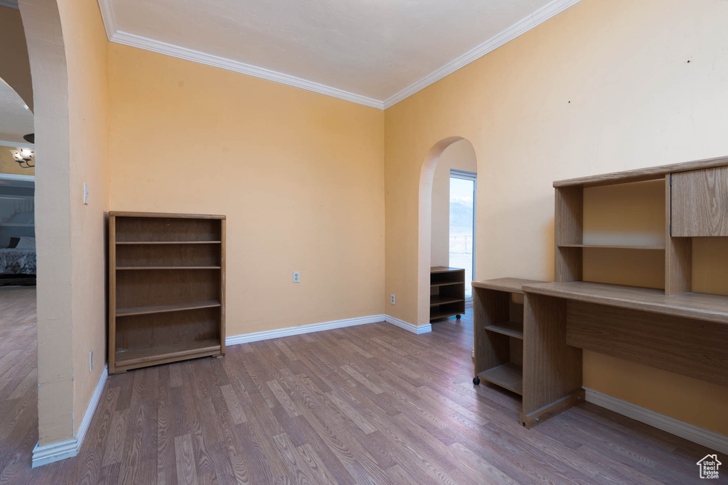 Unfurnished office featuring arched walkways, crown molding, baseboards, and wood finished floors