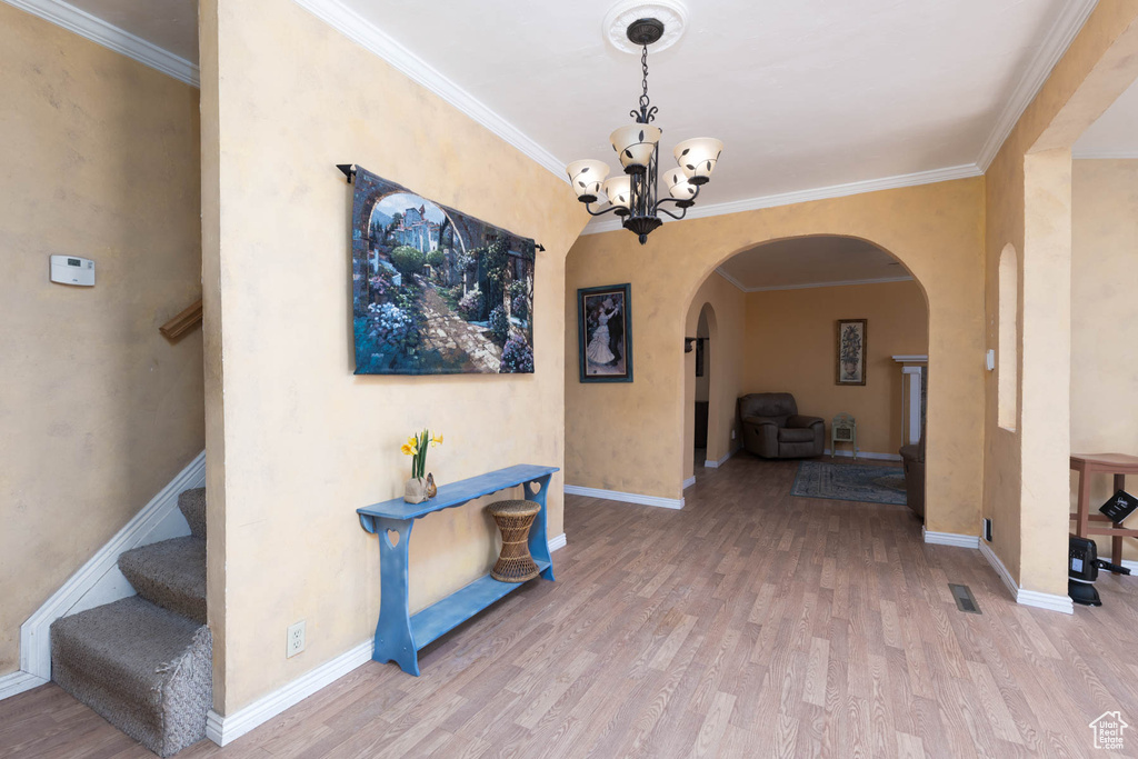 Corridor featuring arched walkways, an inviting chandelier, wood finished floors, and crown molding