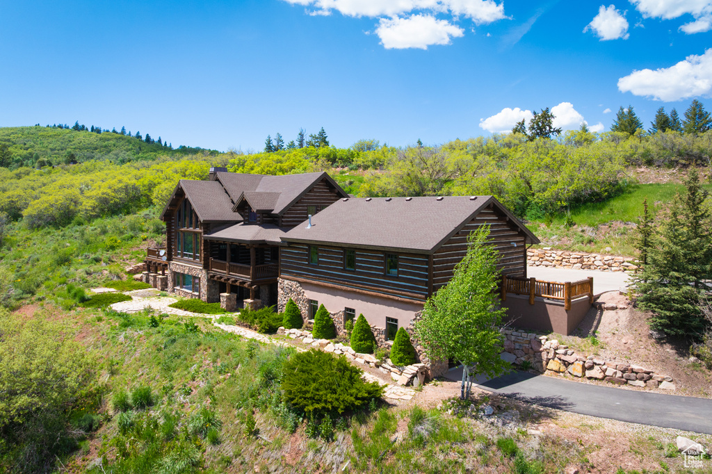 View of front facade featuring log siding, stone siding, a view of trees, and a deck