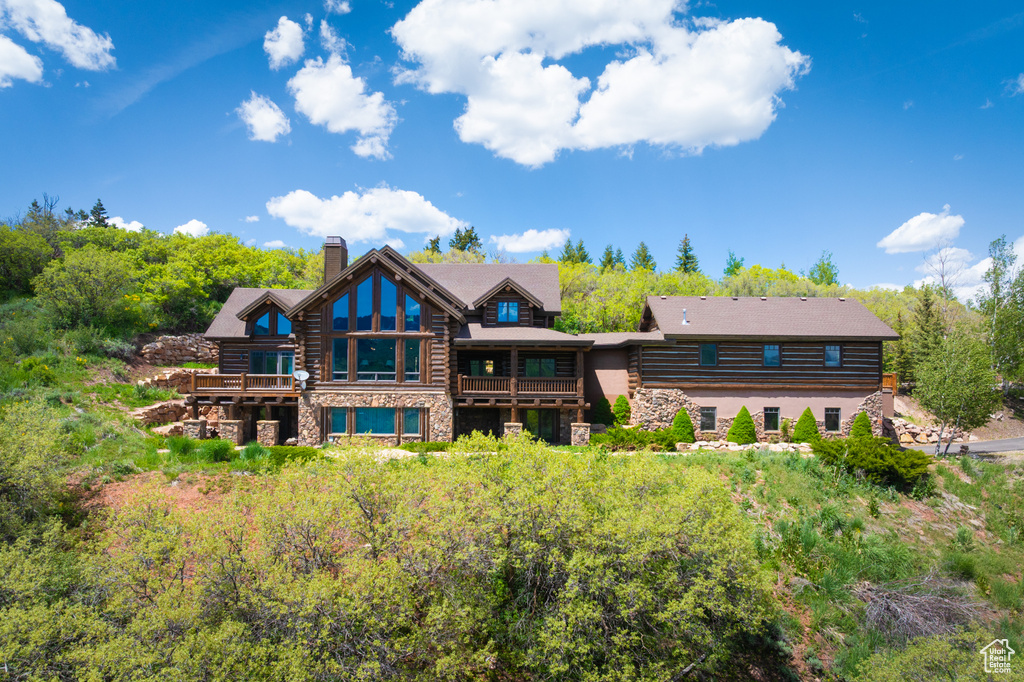 Rear view of property featuring a chimney, stone siding, a balcony, and log exterior