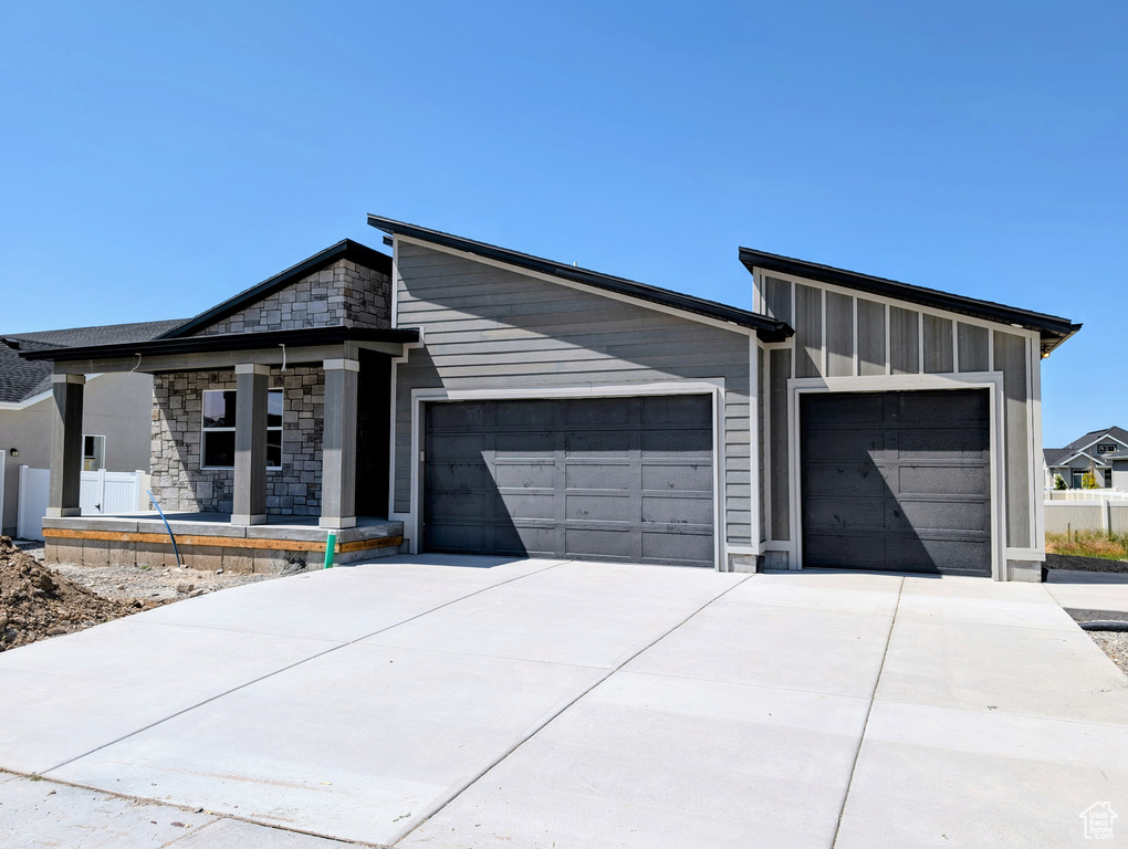 Contemporary house featuring a garage, concrete driveway, stone siding, and covered porch