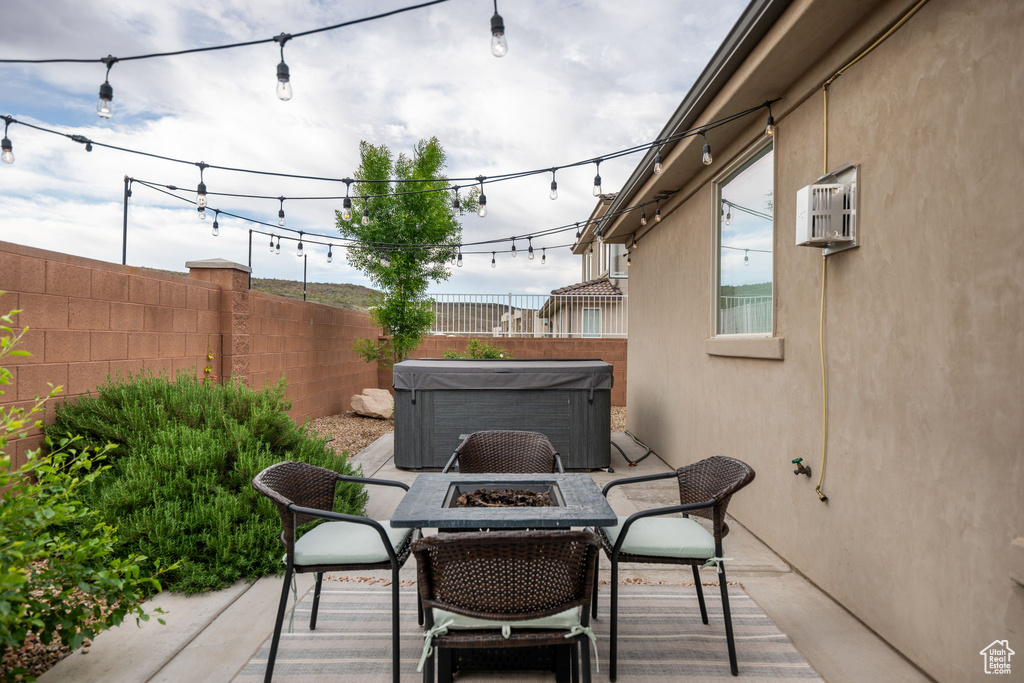 View of patio / terrace featuring an AC wall unit, central AC, fence, a fire pit, and a hot tub