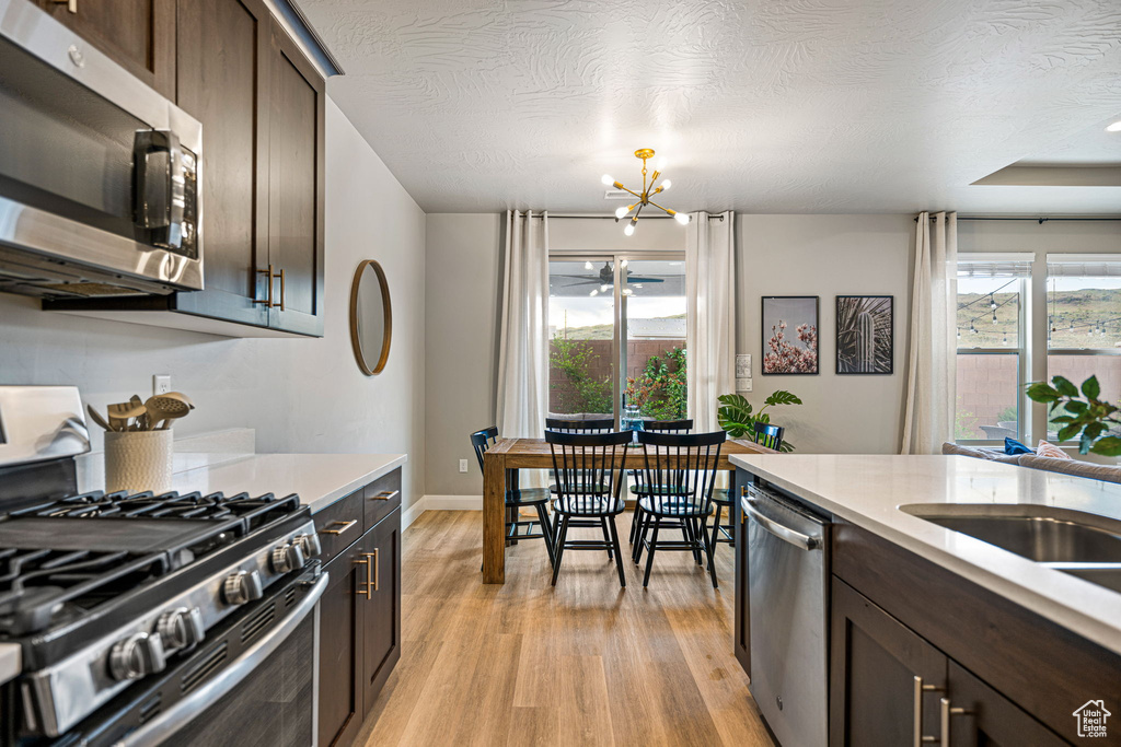 Kitchen with dark brown cabinetry, light wood-style floors, appliances with stainless steel finishes, light countertops, and a chandelier