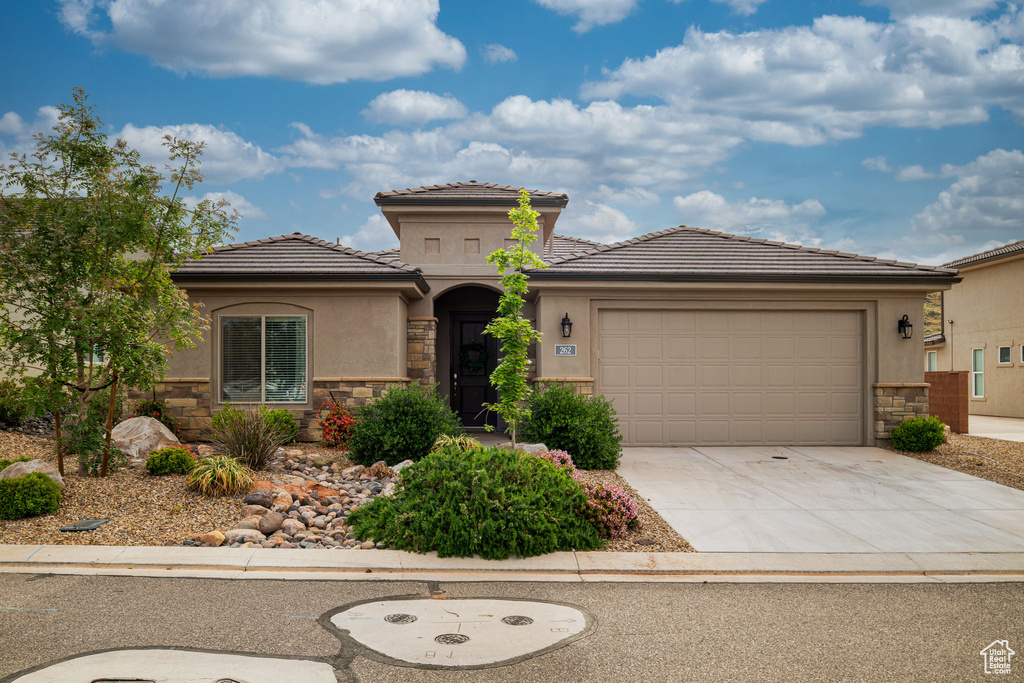 View of front of property featuring stone siding, concrete driveway, an attached garage, and a tile roof
