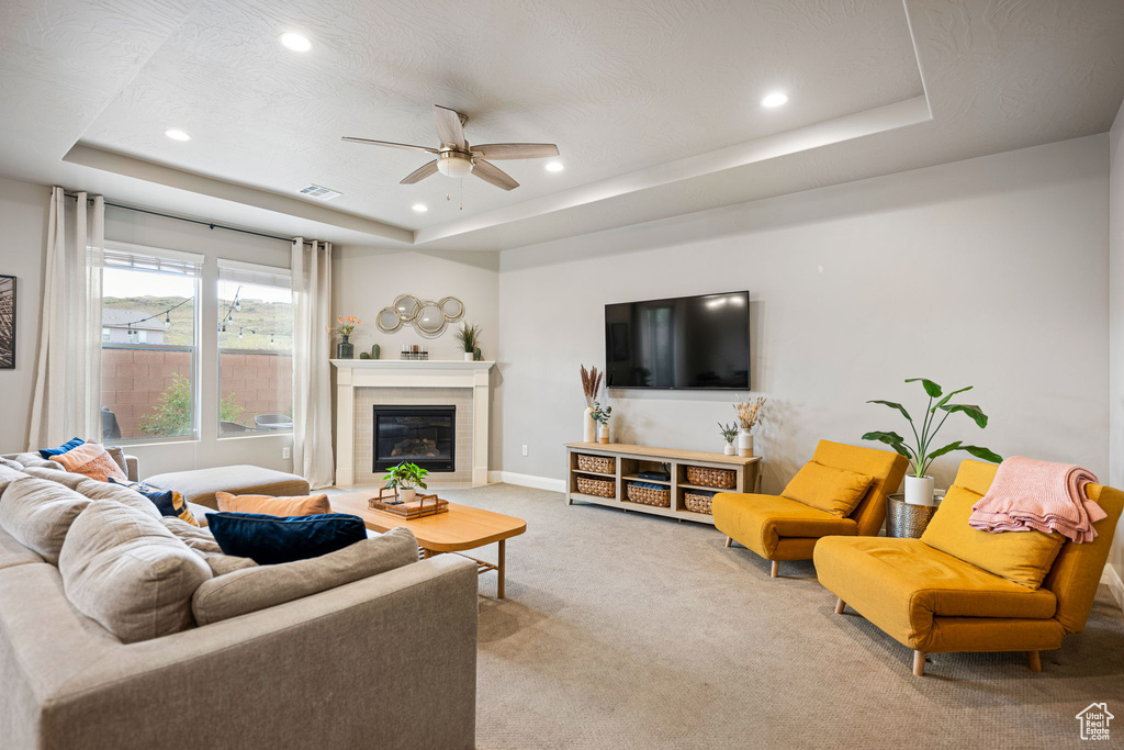 Living room with visible vents, baseboards, ceiling fan, light colored carpet, and a raised ceiling