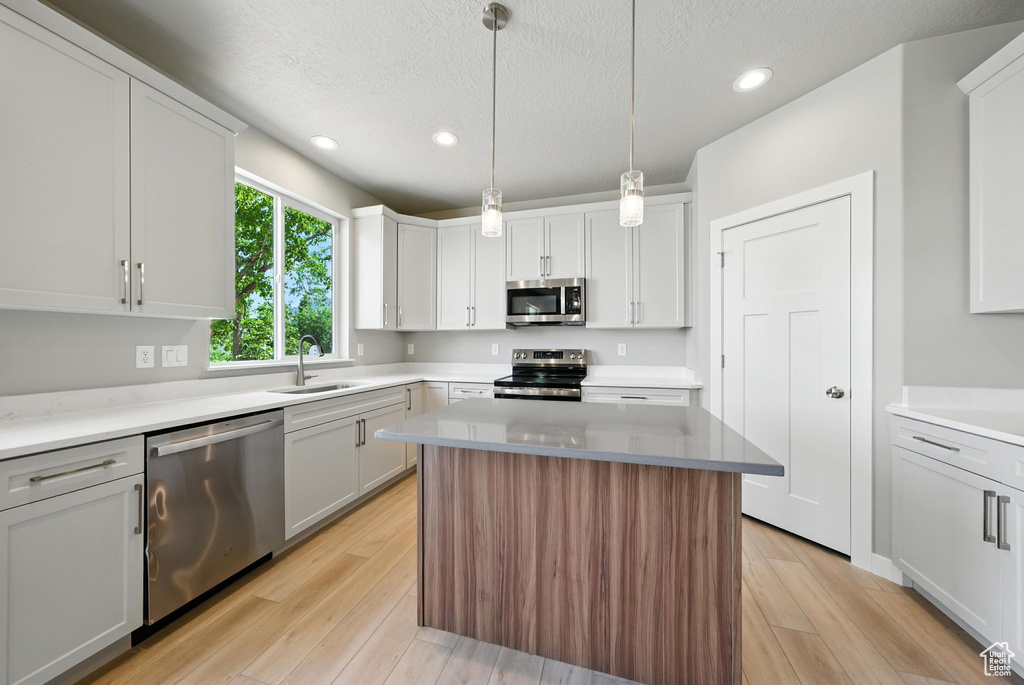 Kitchen with stainless steel appliances, recessed lighting, light wood-style floors, white cabinetry, and a textured ceiling
