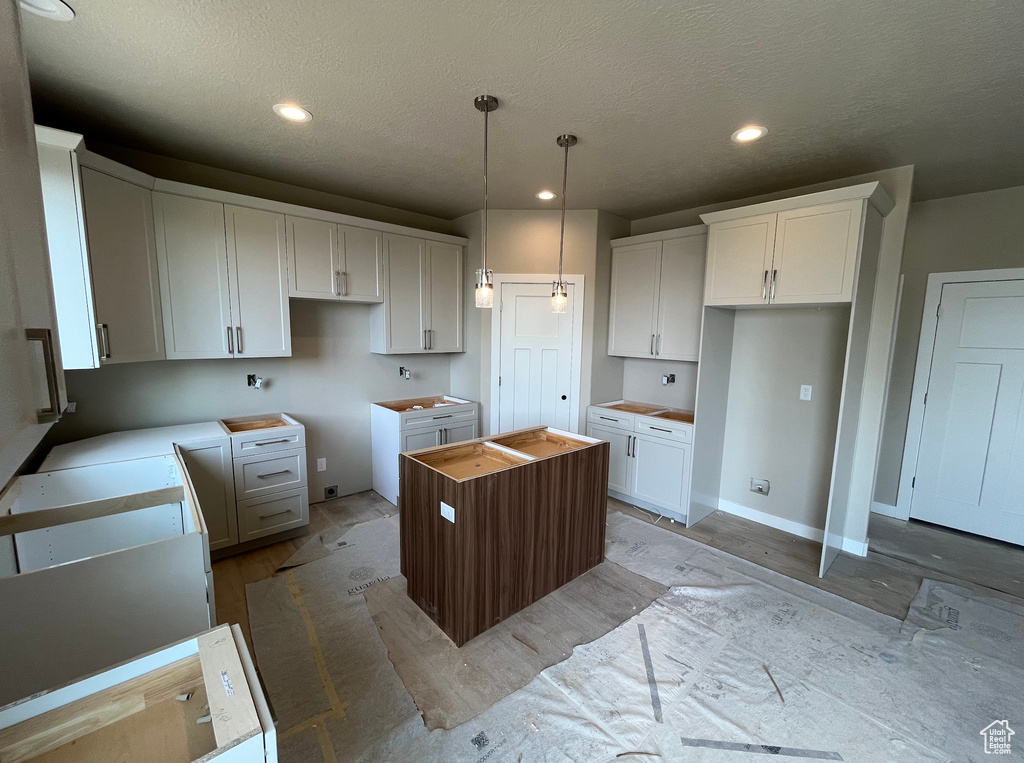 Kitchen featuring a center island, light wood finished floors, a textured ceiling, white cabinetry, and pendant lighting