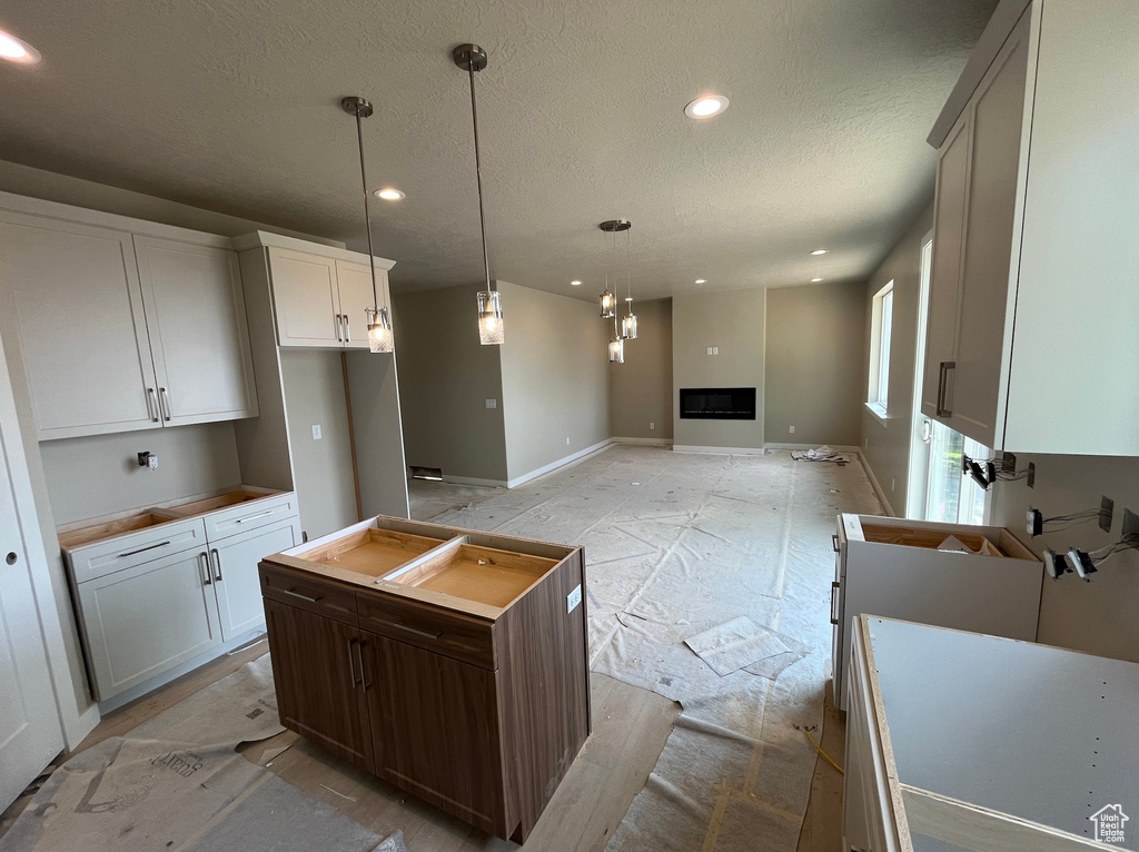 Kitchen featuring recessed lighting, a textured ceiling, a fireplace, hanging light fixtures, and baseboards