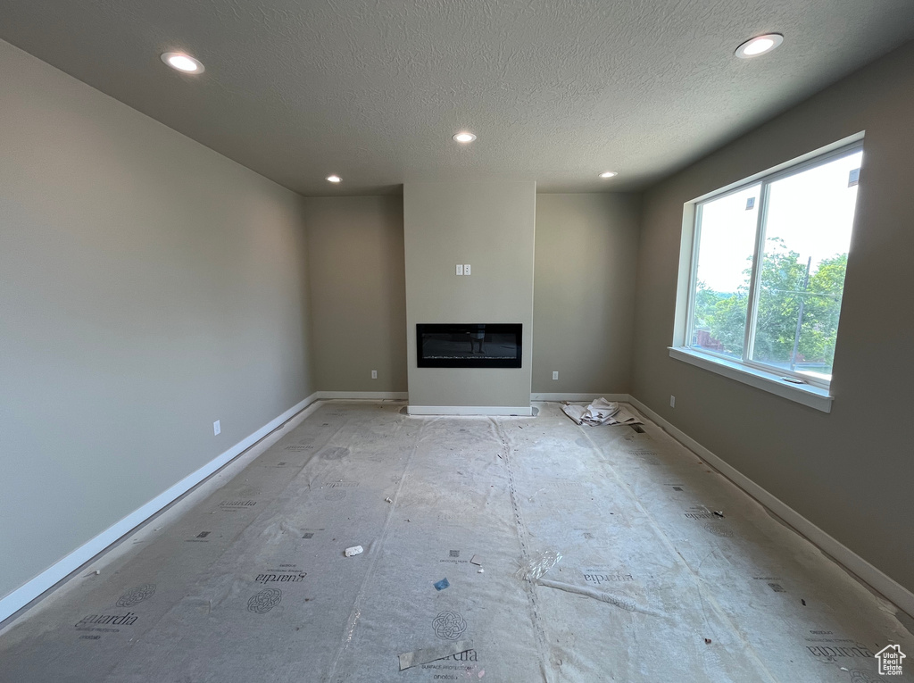Empty room featuring recessed lighting, a glass covered fireplace, a textured ceiling, and baseboards