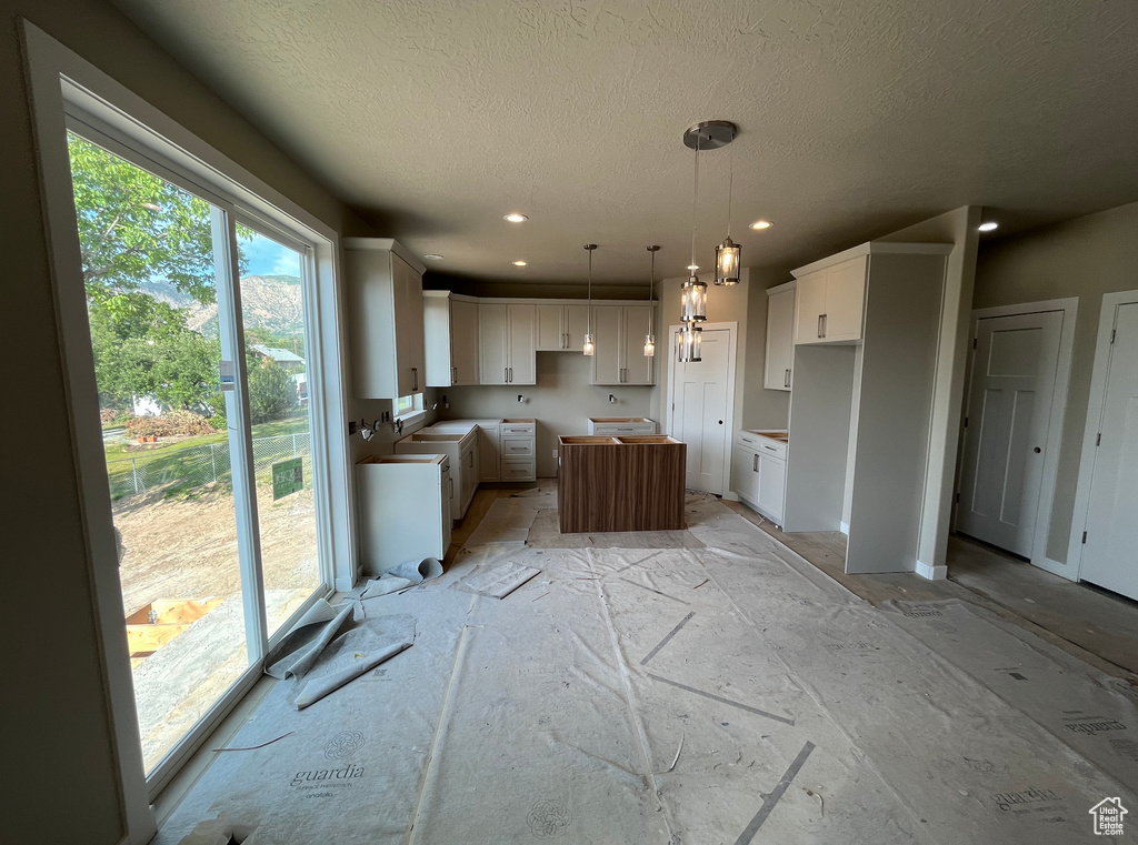 Kitchen featuring a textured ceiling, a kitchen island, white cabinets, pendant lighting, and recessed lighting