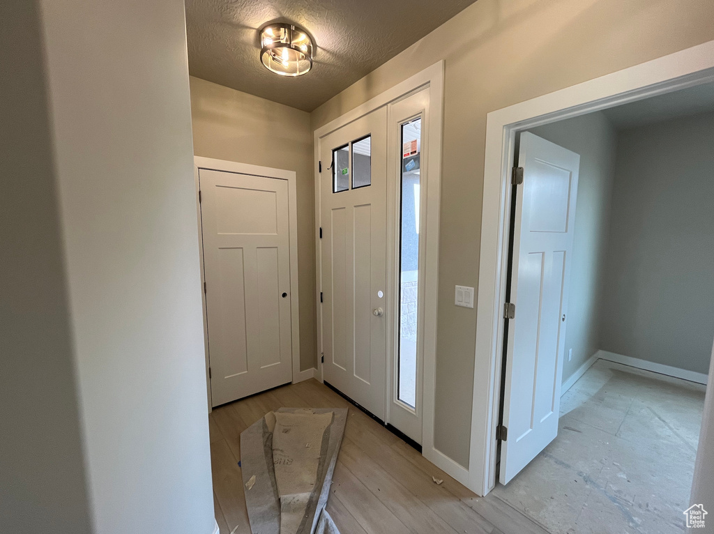Entryway with baseboards, a textured ceiling, and light wood-style flooring