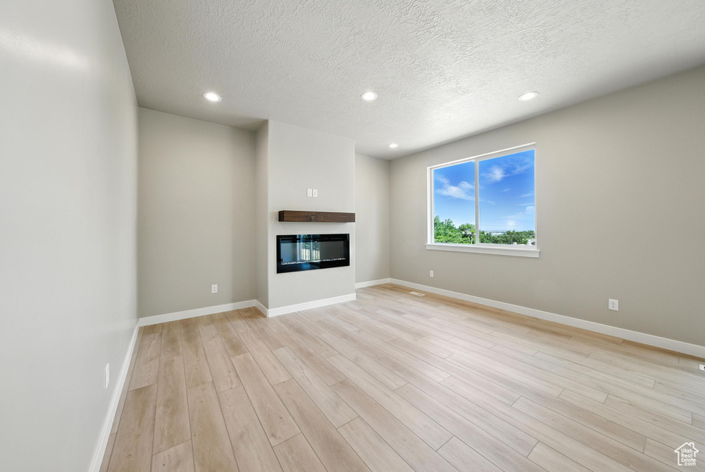 Unfurnished living room featuring light wood-type flooring, a glass covered fireplace, a textured ceiling, and recessed lighting
