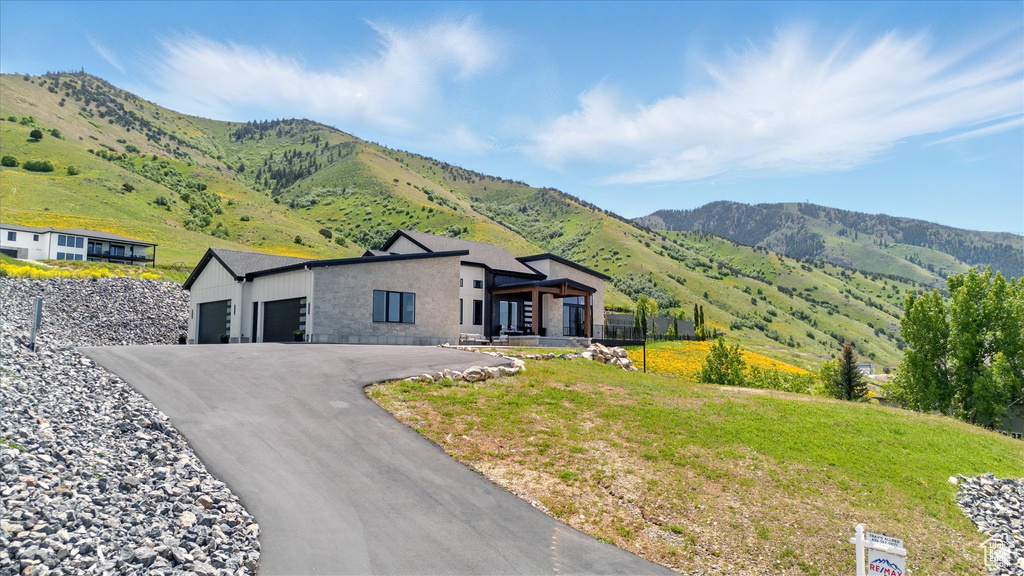 View of front of house with a garage, a mountain view, stone siding, and driveway