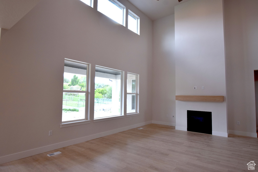 Unfurnished living room with a high ceiling, wood finished floors, a fireplace, and baseboards