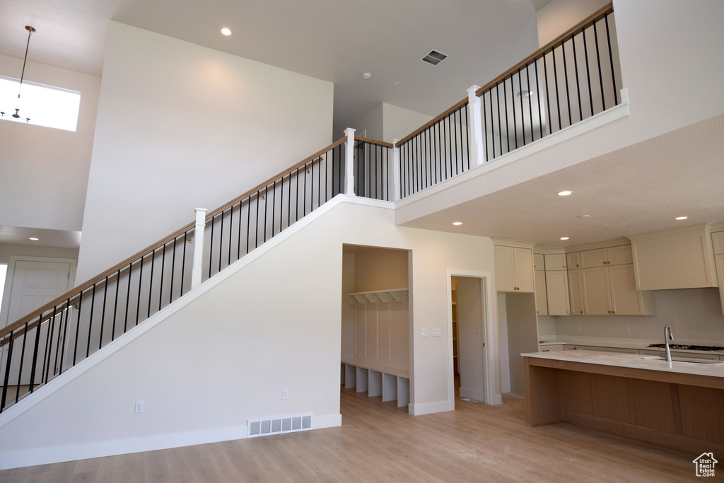 Kitchen with a towering ceiling, a sink, light wood-style floors, recessed lighting, and light countertops