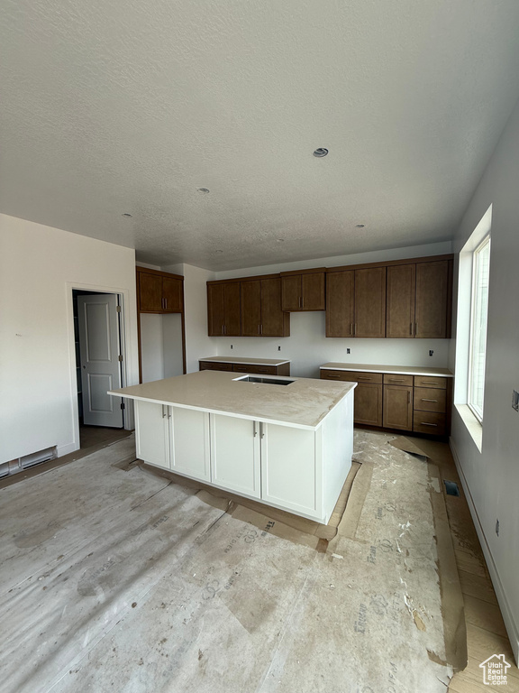 Kitchen with a spacious island, baseboards, light countertops, a sink, and a textured ceiling