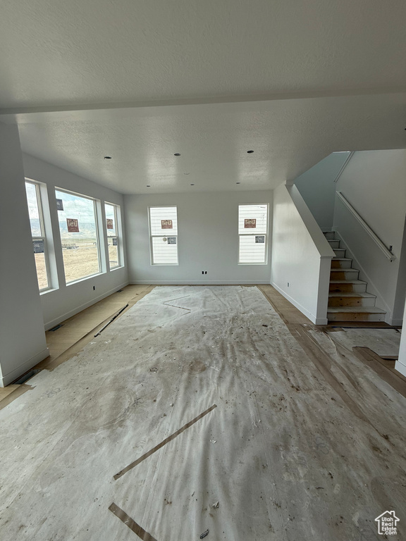 Unfurnished living room featuring plenty of natural light, a textured ceiling, stairs, and baseboards