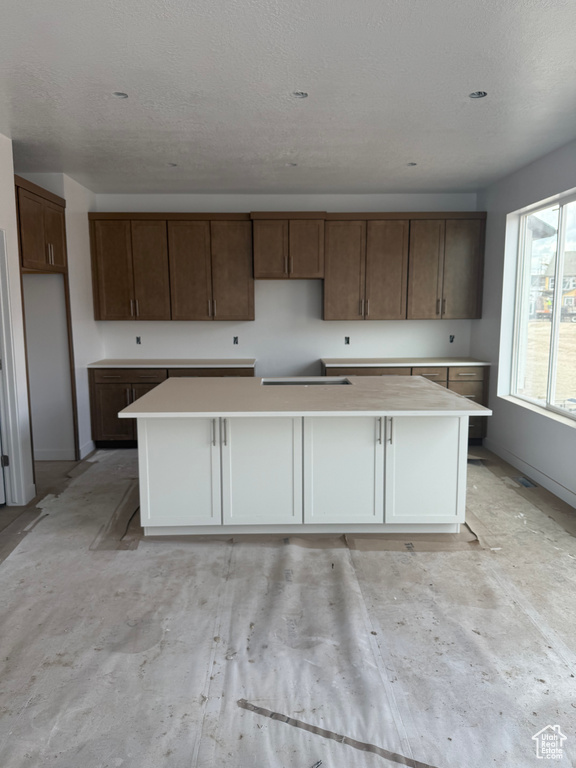 Kitchen featuring a large island, baseboards, a textured ceiling, and light countertops