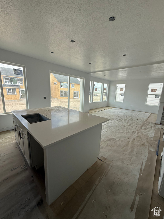 Kitchen featuring a textured ceiling, a center island with sink, light countertops, and open floor plan