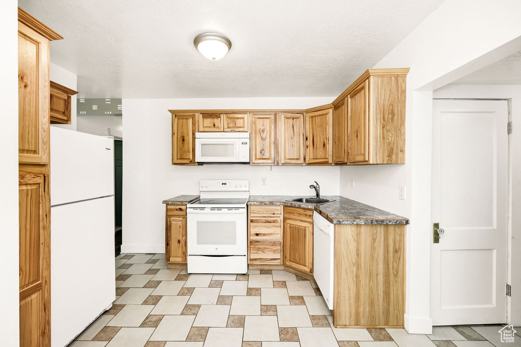 Kitchen with white appliances, a sink, dark countertops, and baseboards