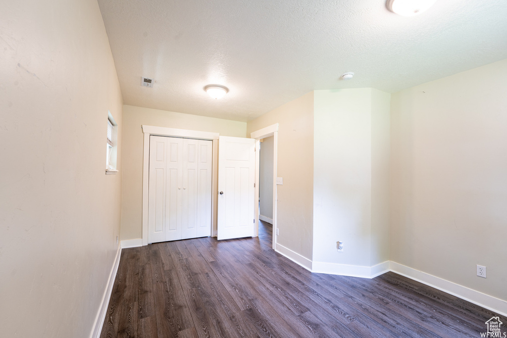 Unfurnished bedroom featuring a closet, dark wood-style floors, baseboards, and a textured ceiling