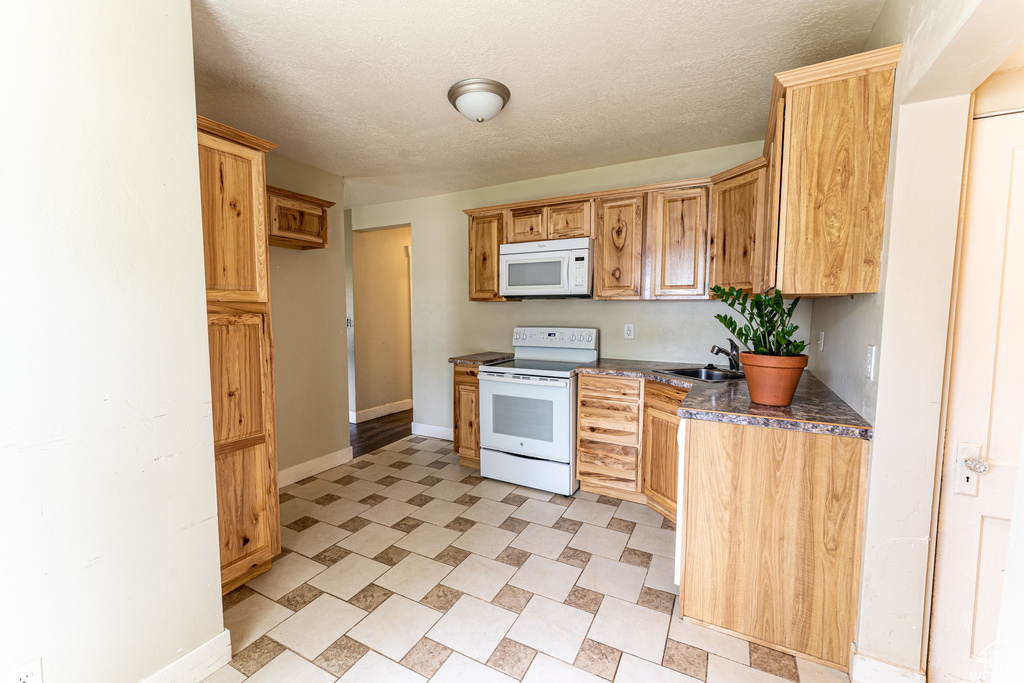 Kitchen with white appliances, baseboards, a textured ceiling, a sink, and dark countertops