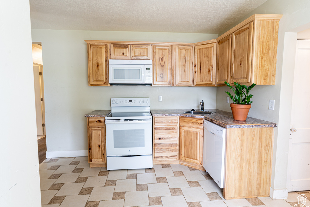 Kitchen featuring a textured ceiling, white appliances, baseboards, light brown cabinets, and a sink