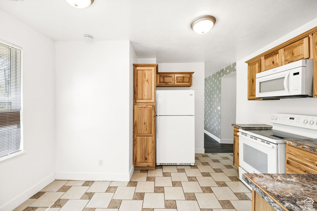 Kitchen with white appliances, baseboards, and dark countertops