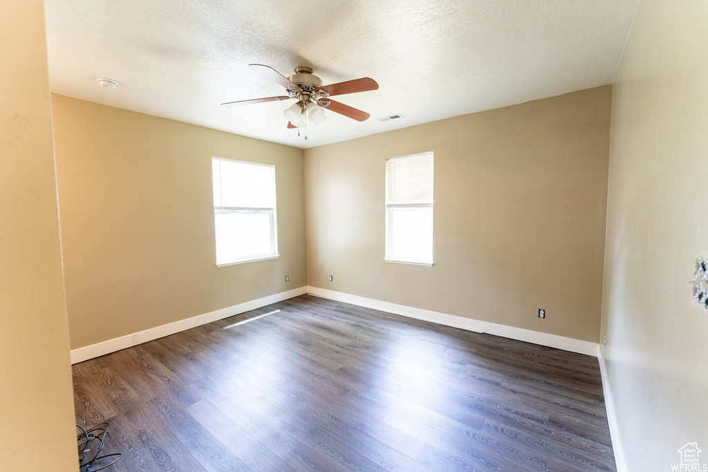 Unfurnished room featuring a ceiling fan, a textured ceiling, baseboards, visible vents, and dark wood-style flooring