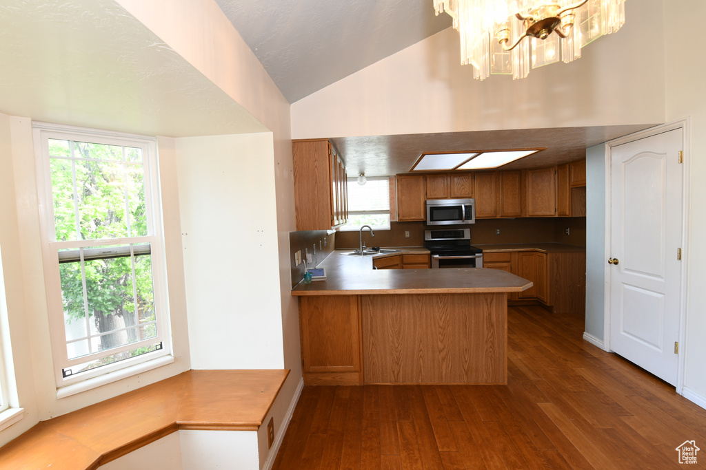 Kitchen featuring stainless steel appliances, brown cabinets, dark wood finished floors, a sink, and lofted ceiling