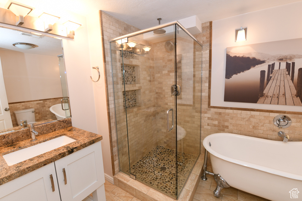 Full bath featuring tile walls, a shower stall, vanity, a freestanding tub, and tile patterned flooring