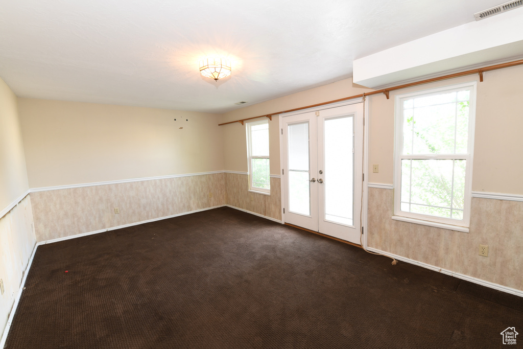 Empty room with french doors, a wainscoted wall, plenty of natural light, and dark carpet