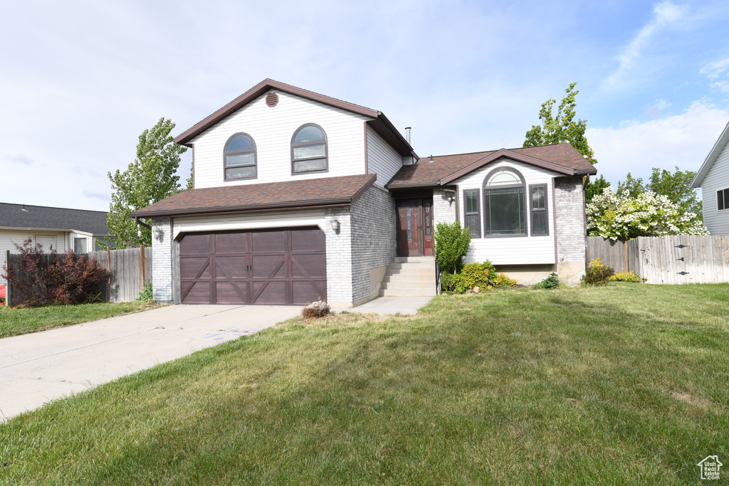 Tri-level home featuring a garage, brick siding, and driveway