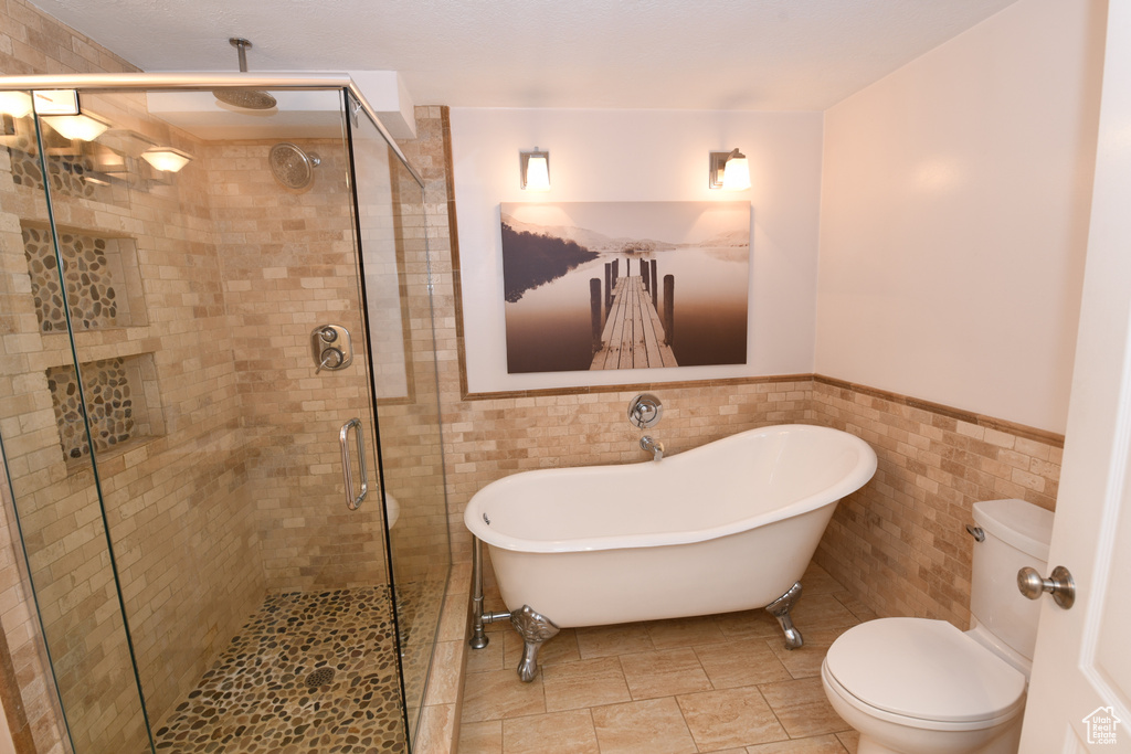 Bathroom with toilet, tile walls, wainscoting, a stall shower, and a soaking tub