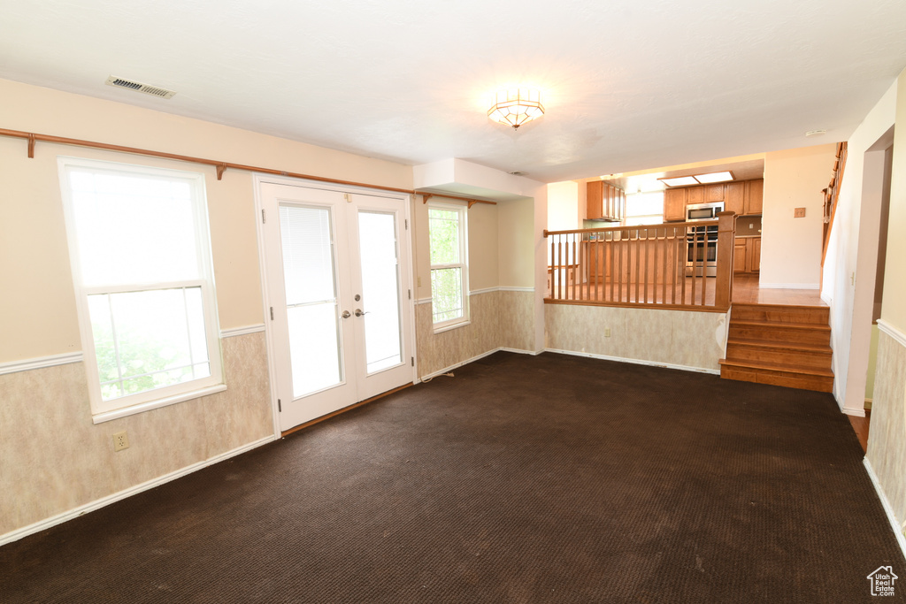 Empty room with healthy amount of natural light, french doors, stairs, and dark carpet