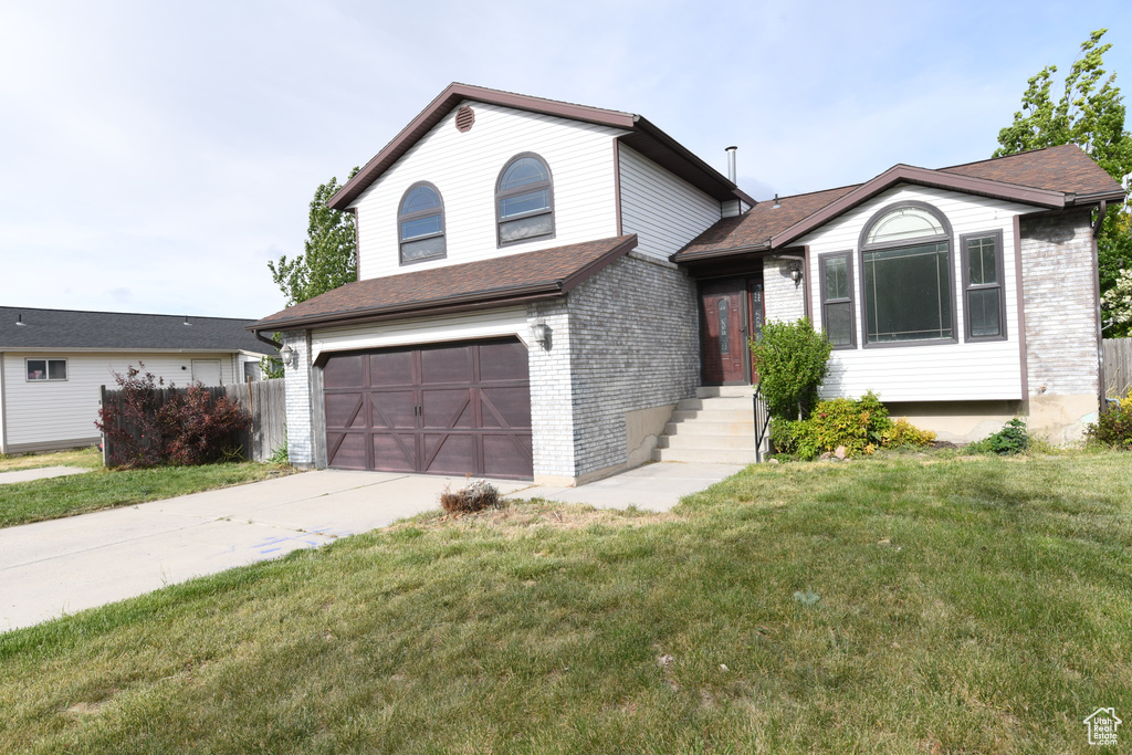 Split level home featuring an attached garage, brick siding, driveway, and a shingled roof