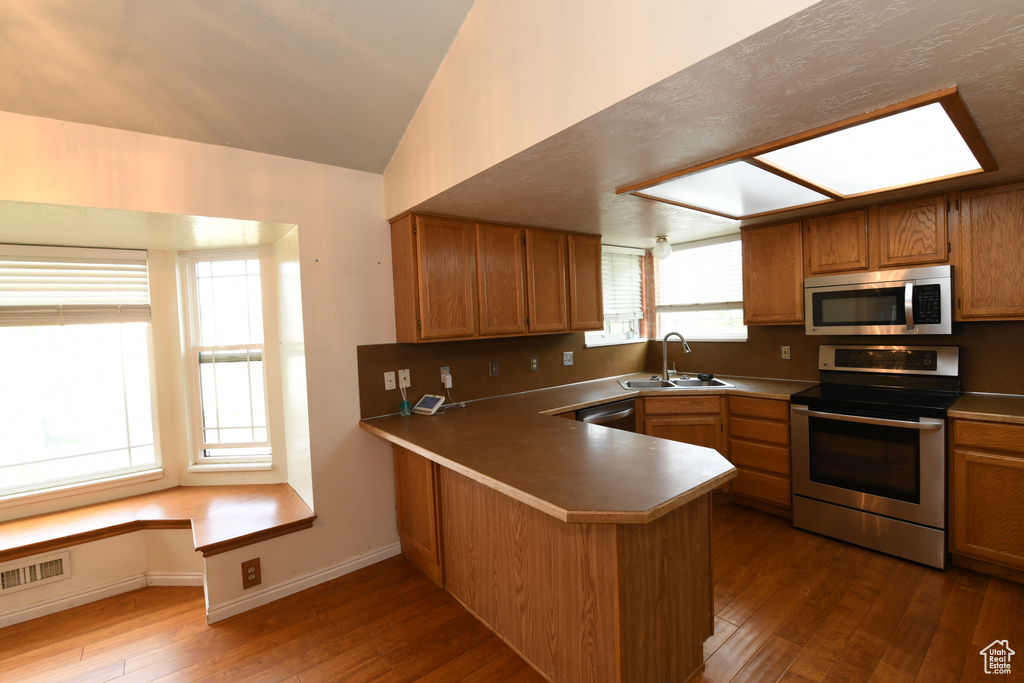 Kitchen featuring stainless steel appliances, a peninsula, a sink, wood finished floors, and vaulted ceiling