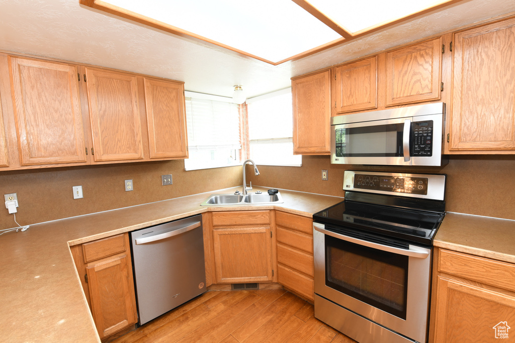 Kitchen featuring stainless steel appliances, a sink, light wood-style flooring, light countertops, and light brown cabinets