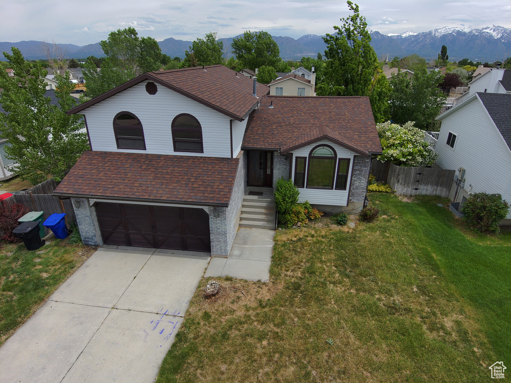 View of front facade with brick siding, a garage, roof with shingles, driveway, and a mountain view