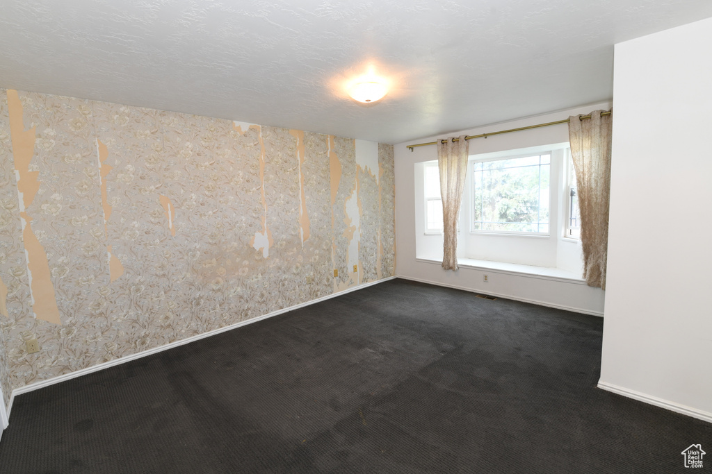 Spare room featuring wallpapered walls, dark colored carpet, and baseboards