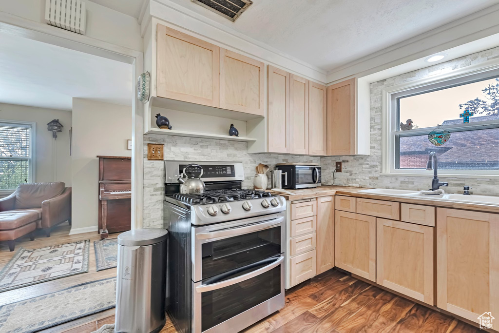 Kitchen with light brown cabinetry, double oven range, a sink, and wood finished floors