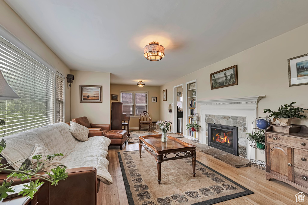 Living room with light wood-style floors, a stone fireplace, and built in shelves